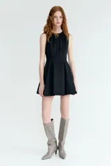Vestido corto sin mangas en denim negro, con escote redondo, cuerpo entallado y falda acampanada con pliegues.