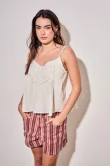 Blusa color off white de algodón peinado, sin mangas, con tirantes finos, escote en V con detalles de encaje y bordados, y pliegues decorativos en los laterales.