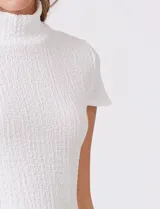 Remera blanca de cuello alto y manga corta, confeccionada en tejido texturizado con relieve tridimensional. Presenta un corte entallado al cuerpo y acabado elástico.