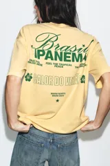 Camiseta amarilla de corte oversize, con cuello redondo, manga corta y estampa frontal en color verde con texto alusivo a Brasil Ipanema y pequeños símbolos.