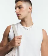 Musculosa básica para hombre de corte recto y cuello redondo, confeccionada en tejido de algodón. Presenta un diseño liso con un pequeño tag decorativo en el bajo.