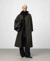 Abrigo largo de color verde militar con corte recto y tejido de efecto encerado. Posee cuello italiano de pana en contraste, cierre frontal oculto por solapa y bolsillos laterales inclinados.