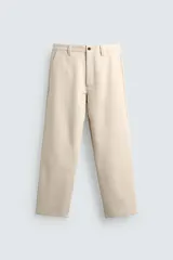 Pantalón chino de corte relajado, confeccionado en tejido estructurado de color beige. Presenta bolsillos frontales, bolsillos traseros de vivo y cierre frontal con cremallera y botón.