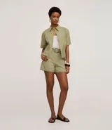 Short de cintura alta confeccionado en cambraia de algodón color verde. Presenta un diseño con ruedo festoneado, trabillas en la cintura y cierre tradicional. Incluye un cinturón al tono con hebilla redonda decorada con pequeños abalorios.