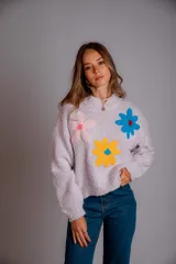 Buzo de punto color lila, con cuello redondo, mangas largas y diseño holgado. Presenta tres flores bordadas en el frente: una rosa claro, una azul y una amarilla con centro azul.