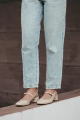 Zapato estilo Mary Jane con diseño destalonado, confeccionado en cuero color beige. Presenta una tira fina con hebilla metálica sobre el empeine, punta redondeada y taco cuadrado forrado de 6 cm de altura.