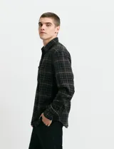 Camisa de franela a cuadros con cuello button-down, manga larga y botones de madera. Presenta dos bolsillos tipo parche en el frente con cierre de botón.