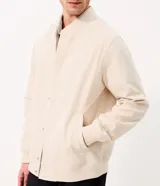 Campera bomber masculina de terciopelo cotelé color beige, con cuello redondo, mangas largas, cierre frontal de botones forrados, bolsillos laterales y terminaciones de elástico en puños y cintura.