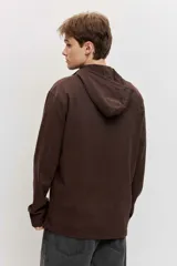 Buzo de friza de algodón marrón con capucha, cuello tipo polo con botones y un bolsillo frontal con solapa en el pecho.