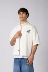 Camisa de manga corta negra, de corte boxy, con cuello camisero, cierre frontal de botones y bordado circular en el pecho.