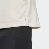 Musculosa deportiva Adidas de corte holgado (boxy) y largo recortado (cropped), color beige claro, con cuello redondo y aberturas amplias en las sisas. Presenta el logo de Adidas Badge of Sport en blanco en el pecho.