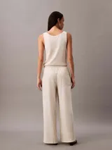 Pantalón de pierna ancha color beige, confeccionado en lino y algodón. Presenta cintura elástica con cordón ajustable, dos bolsillos laterales y un bolsillo trasero.