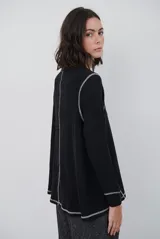 Remera de manga larga en color beige, confeccionada en tejido de punto con costuras a la vista en contraste. Presenta un corte holgado, cuello redondo y un pequeño bordado distintivo en la parte inferior.