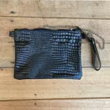 Sobre negro con textura tipo piel de cocodrilo, confeccionado en cuero vacuno. Tiene forro interior, bolsillo interno, correa de cadena desmontable y agarradera de cuero.
