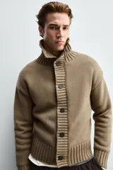 Chaqueta de punto de corte relajado, color marrón, con cuello subido, manga larga y cierre frontal de botones. Presenta acabados en rib en puños y ruedo.