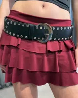 Cinturón negro de cuero sintético con diseño de tachas metálicas plateadas a lo largo de toda la tira y hebilla metálica grande de diseño redondeado.