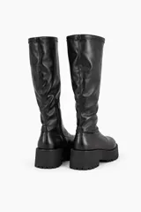 Bota de caña alta color negro, confeccionada en material sintético con acabado mate. Presenta una suela de plataforma track con taco cuadrado y cierre lateral interno.