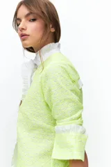 Camisa de manga larga confeccionada en broderie de algodón con bordados en hilo flúo color naranja. Presenta cuello mao, cartera frontal con volados y puños con volados.