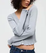 Cardigan de punto texturizado color rosado, con escote en V, cierre frontal por botones, mangas largas y acabado con volados sutiles en el ruedo y los puños.