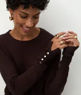 Suéter de punto ajustado con cuello redondo y manga larga. Presenta detalle de botones metalizados en los puños.