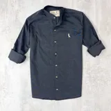 Camisa gris oscura de algodón con cuello mao, manga larga con puños enrollados, cierre frontal con botones y logo bordado en el pecho.