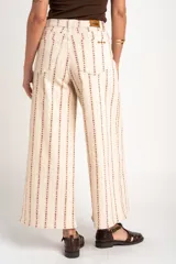 Pantalón de jean tiro alto y corte wide leg, en color beige con estampado vertical de líneas y motivos florales en tono marrón.