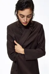 Blazer de botonadura sencilla color marrón oscuro con solapas de muesca, cierre de un botón, hombreras y bolsillos delanteros ribeteados.