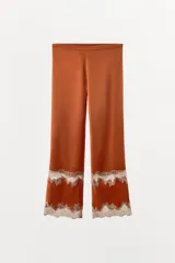 Pantalón de tiro medio confeccionado en tejido satinado, con cintura elástica y pernera recta. Presenta detalles de encaje y bordados en contraste en el ruedo.