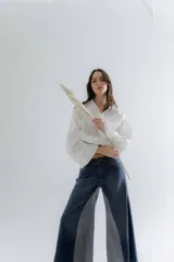 Jean de corte oxford con tiro medio-alto, confeccionado en algodón. Presenta un diseño de paneles con cortes verticales en dos tonos de azul y costuras marcadas en las piernas, ofreciendo una silueta amplia y fluida.