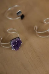 Pulsera abierta de metal plateado con diseño minimalista de doble banda y piedra natural de amatista engarzada en el centro.