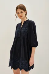 Vestido corto de viscosa color negro, con diseño holgado, mangas tres cuartos abullonadas y cuello en V. Presenta delicados bordados florales en tono azul oscuro en el pecho y en el ruedo, el cual termina con un borde festoneado.