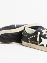 Zapatilla Golden Goose modelo Super-Star de estilo urbano con efecto desgastado. Presenta cuerpo de cuero blanco, estrella lateral con glitter plateado, talón en tono gris texturizado y forro interior de corderito sintético.