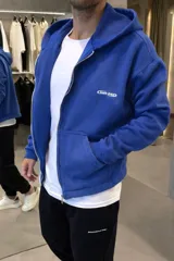 Campera con capucha y cierre frontal, de corte boxy y color azul vibrante. Presenta bolsillos tipo canguro y un pequeño logo bordado en el pecho.