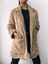 Saco de abrigo color beige, de textura suave tipo peluche, con cuello solapa, cierre frontal con botones y bolsillos laterales.