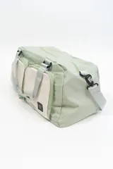 Bolso deportivo color rosa con detalles en beige y gris. Tiene doble asa de mano y correa de hombro ajustable. Cuenta con dos bolsillos frontales con cierre y logo de la marca en la esquina inferior derecha.