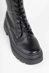 Borcego negro de caña media en símil cuero, con interior acolchonado, cordones a tono, cierre en uno de sus laterales y plataforma tipo tractor de 6cm de alto.