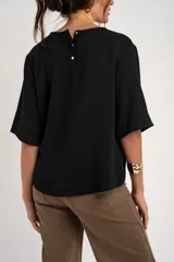 Blusa negra de manga corta y cuello redondo, confeccionada en tejido ligero y fluido.