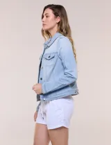 Camperita de denim clásico con lavado claro, cuello camisero, cartera frontal con botones metálicos y bolsillos superiores con solapa. Presenta mangas largas con puños abotonados y costuras estructuradas.