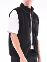 Chaleco de polar tipo corderito en color beige, con cuello alto y cierre frontal completo. Presenta un bolsillo de parche en el pecho en color azul marino con cierre de cremallera y ribetes en contraste en el mismo tono en sisas, cuello y bolsillos laterales.