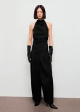 Top de fiesta con cuello halter y diseño drapeado. Presenta un corte recto con bajo asimétrico y cierre de botones en la parte posterior del cuello.