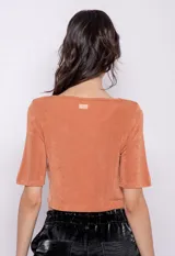 Top color rosa nude, de manga corta y escote redondo con abertura en forma de gota y nudo en la parte central. Confeccionado en tela con pequeños destellos metálicos.