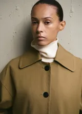 Chaqueta de corte amplio en tono tostado, con solapas y cuello de cuero sintético en color negro kontrastante. Posee cierre frontal de botones oscuros y bolsillos laterales discretos.