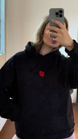 Canguro negro de algodón con felpa, de corte holgado, con capucha y bolsillo frontal tipo canguro. Presenta un bordado en la parte delantera y un aplique de piedras rojas en forma de corazón.