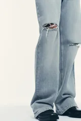 Jeans de tiro bajo, pierna ancha y largo completo, color celeste claro con efecto desgastado y rotos a la altura de las rodillas.