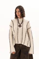Buzo tejido de punto con silueta relajada, cuello alto y mangas tipo campana. Presenta un diseño de trenzas verticales con detalles de costuras en contraste a lo largo de la prenda.