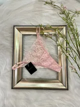 Pack de tres tangas de encaje con diseño floral, breteles regulables y laterales finos. El conjunto incluye una tanga rosa claro, una tanga color tostado con bordes grises y una tanga roja.