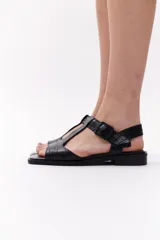 Sandalias negras de cuero con diseño de tiras en forma de T y hebilla lateral.