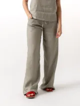 Pantalón largo de lino color gris, de corte holgado, con cintura elástica ajustable con cordón, dos bolsillos laterales y un bolsillo trasero.