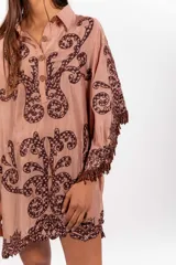 Vestido corto de silueta amplia, color tostado con bordados barrocos en contraste, escote en V con botones de madera, mangas anchas tipo capa con flecos de cuentas en los bordes.