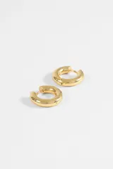 Aros tipo argolla de diseño grueso y compacto, fabricados en acero quirúrgico con acabado dorado.